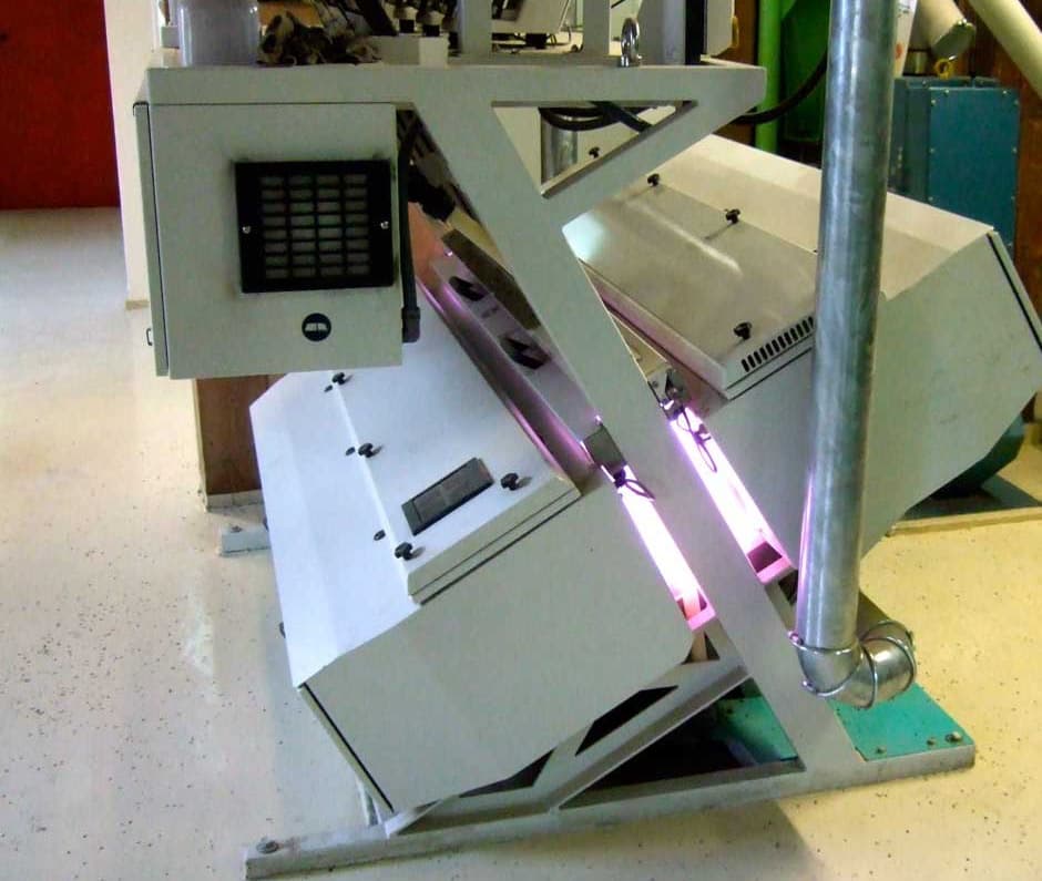 Chute-type optical sorter for grains, seeds and nuts in a mill, with its inspection lights glowing between the two halves