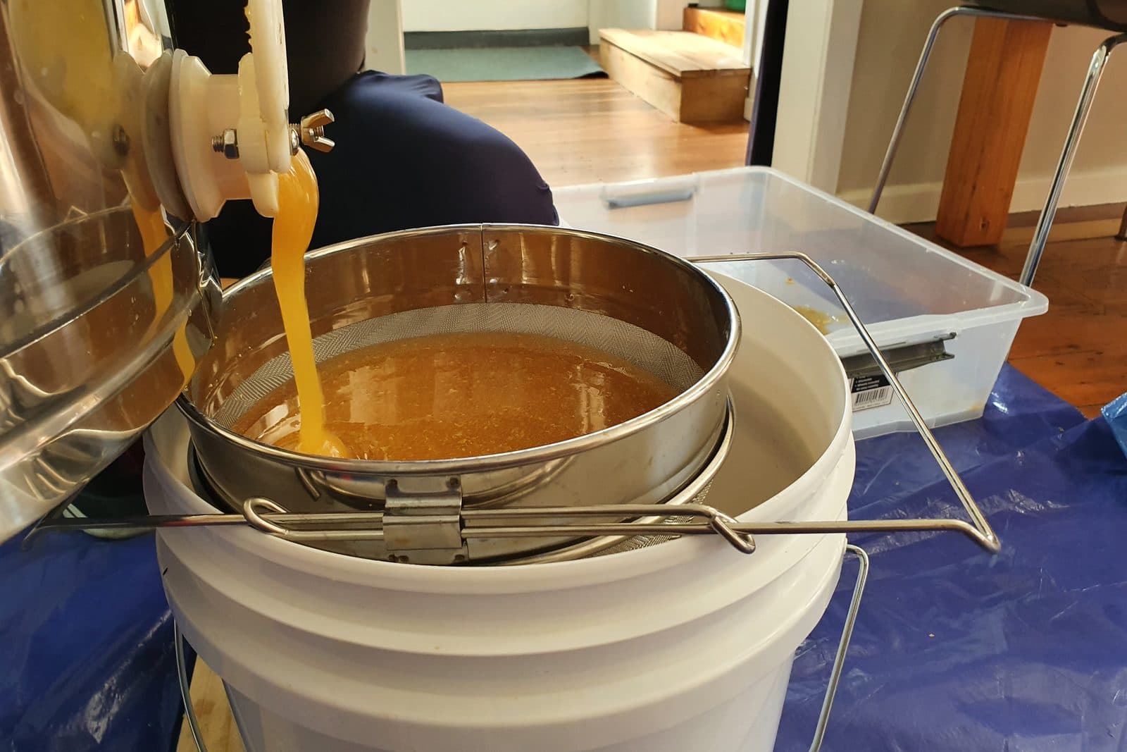 Honey running from the gate of a stainless-steel extractor into a double sieve on a bucket